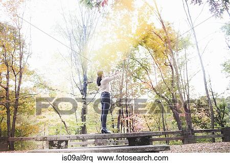 Stock Photography - Young woman standing on picnic bench photographing autumn forest with smartphone. Fotosearch