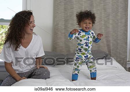 Young woman watching toddler son jumping on bed View Large Photo Image Stock Photograph - Young woman watching toddler son jumping on bed. Fotosearch
