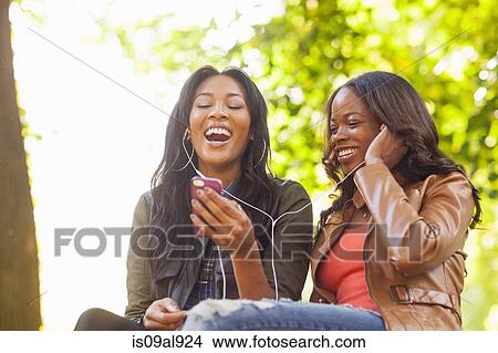 Young women using smartphone together in park View Large Photo Image Picture - Young women using smartphone together in park. Fotosearch