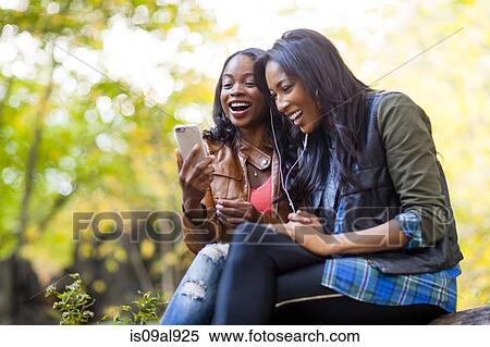 Young women using smartphone together in park View Large Photo Image Stock Photography - Young women using smartphone together in park. Fotosearch