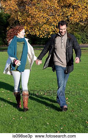 Stock Photography - A mid adult couple hold hands in dulwich park. Fotosearch
