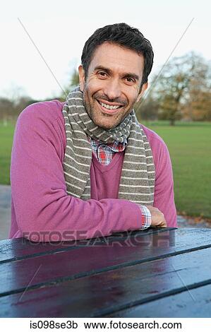 Stock Image - A mid adult man sitting at a table in dulwich park. Fotosearch