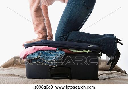 A woman kneeling on a suitcase full of clothes View Large Photo Image Stock Photo - A woman kneeling on a suitcase full of clothes. Fotosearch