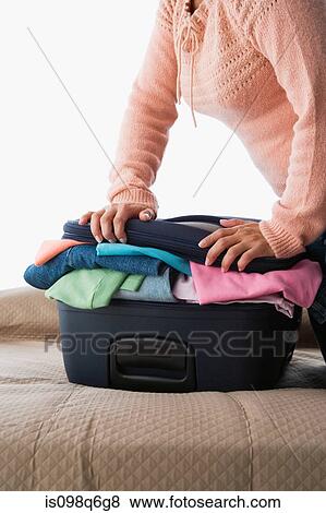 A woman pressing on a suitcase full of clothes View Large Photo Image Stock Photo - A woman pressing on a suitcase full of clothes. Fotosearch