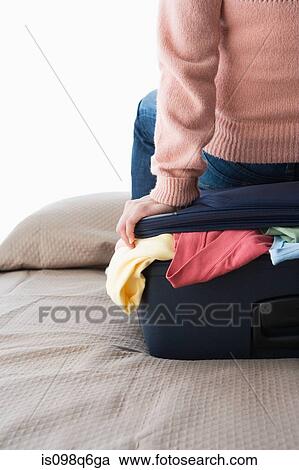 A woman sitting on a suitcase full of clothes View Large Photo Image Stock Image - A woman sitting on a suitcase full of clothes. Fotosearch