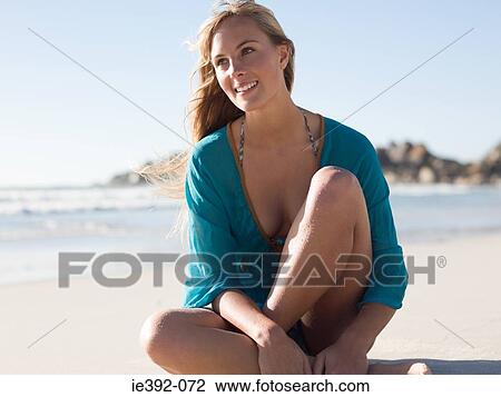 Stock Image - A young woman sitting on a beach. Fotosearch