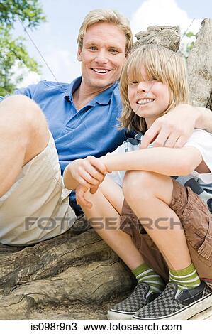 Stock Image - Boy and father sitting on tree trunk. Fotosearch