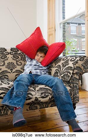 Stock Image - Boy covering his ears with cushions. Fotosearch