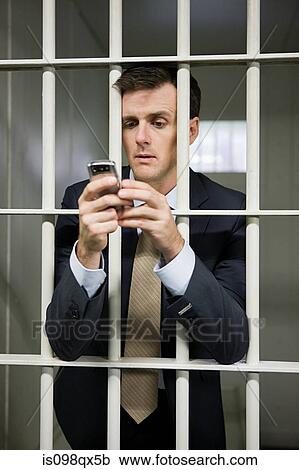 Stock Image - Businessman in cell with cellphone. Fotosearch