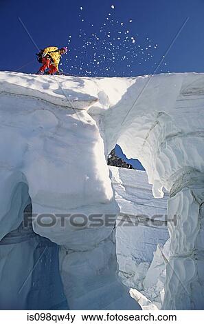 Stock Photo - Climber crossing snow bridge on coleman glacier. Fotosearch