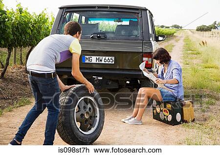 Stock Image - Couple by suv with tyre and map. Fotosearch