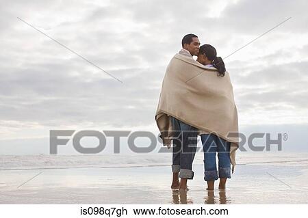 Stock Image - Couple in blanket by the sea. Fotosearch