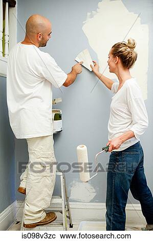Stock Image - Couple painting wall, woman holding color swatch. Fotosearch