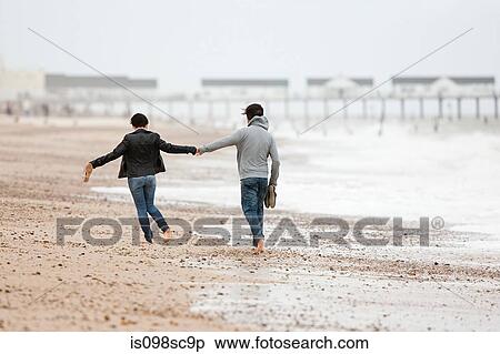 Stock Photography - Couple running hand in hand by the sea. Fotosearch