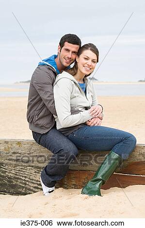 Stock Photograph - Couple sitting on a fence at the beach. Fotosearch