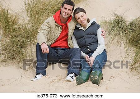 Stock Image - Couple sitting on a sand dune. Fotosearch