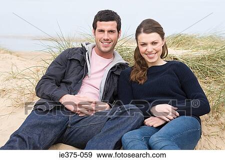 Couple sitting on a sand hill at beach View Large Photo Image Stock Photo - Couple sitting on a sand hill at beach. Fotosearch