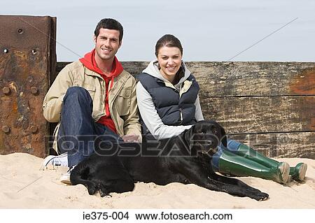 Picture - Couple sitting with pet dog at beach. Fotosearch