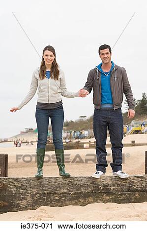 Stock Image - Couple standing on a fence at beach. Fotosearch