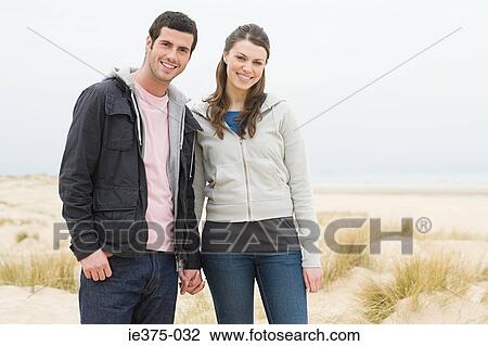 Stock Image - Couple standing on a sandy beach. Fotosearch