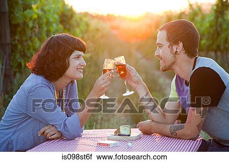 Stock Image - Couple toasting with glasses of wine in field. Fotosearch
