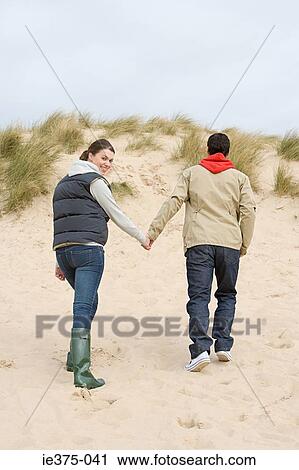 Stock Image - Couple walking up a sandy hill. Fotosearch
