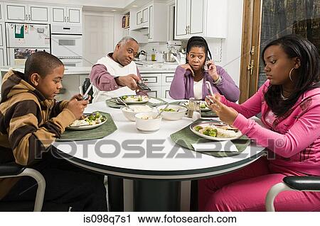 Stock Image - Distracted family at the dinner table. Fotosearch