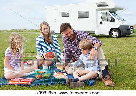 Stock Image - Family having picnic by caravan. Fotosearch