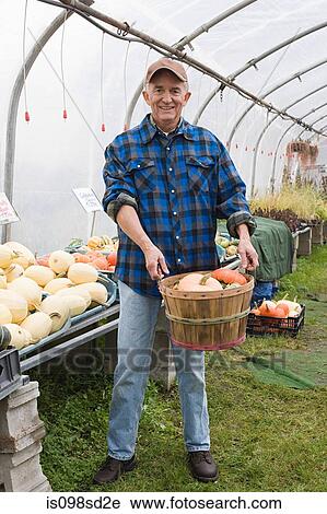 Stock Image - Farmer in greenhouse with pumpkin. Fotosearch