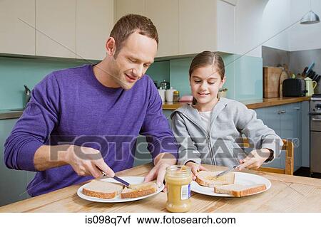 Stock Image - Father and daughter spreading peanut butter on bread. Fotosearch