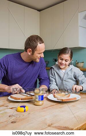 Stock Photo - Father and daughter spreading peanut butter on bread. Fotosearch