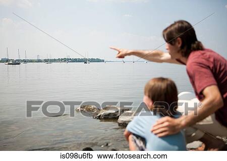 Stock Image - Father and son on beach, father pointing across harbor. Fotosearch