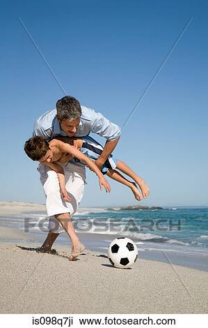 Stock Image - Father and son playing football by the sea. Fotosearch