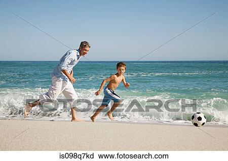 Stock Image - Father and son playing football by the sea. Fotosearch