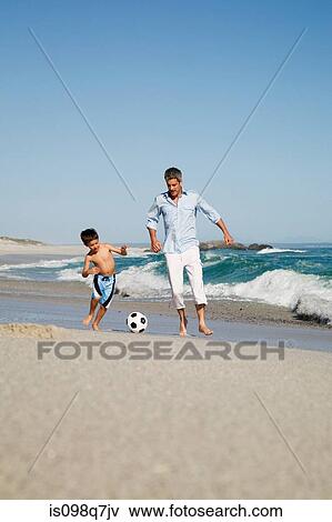 Stock Photo - Father and son playing football by the sea. Fotosearch