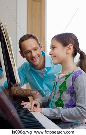 Stock Image - Father teaching daughter how to play the piano. Fotosearch
