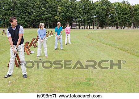 Stock Image - Four golfers on a driving range. Fotosearch