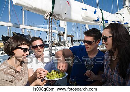 Picture - Friends eating grapes on a boat. Fotosearch