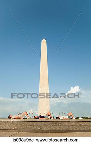 Stock Image - Friends lying down by washington monument. Fotosearch