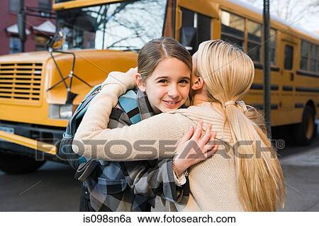 Stock Image - Girl and mother hugging by school bus. Fotosearch