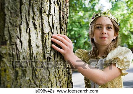 Stock Photograph - Girl dressed up as queen touching tree trunk. Fotosearch