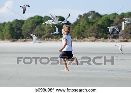 Stock Image - Girl running on beach amongst seagulls. Fotosearch