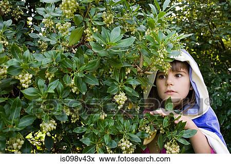 Stock Photo - Girl wearing cape with hood hiding in bushes. Fotosearch