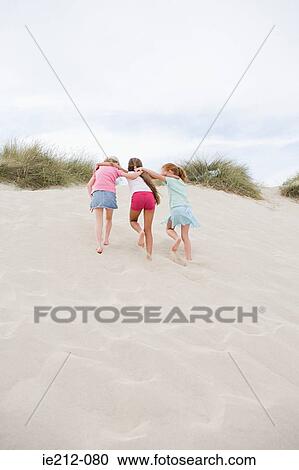 Stock Image - Girls walking up a sand dune. Fotosearch