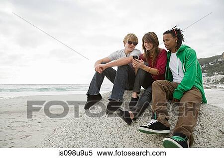 Stock Photography - Group of friends sitting on boulder. Fotosearch