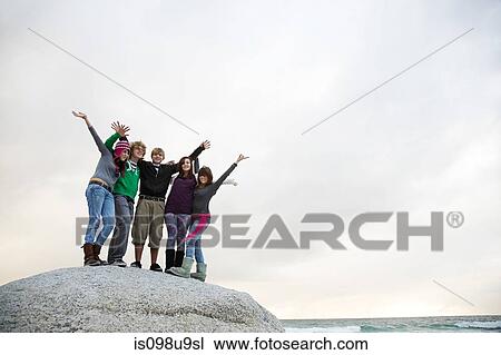 Stock Image - Group of friends standing on boulder. Fotosearch