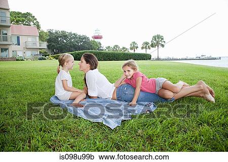 Stock Image - Happy mother and daughters lying on grass. Fotosearch