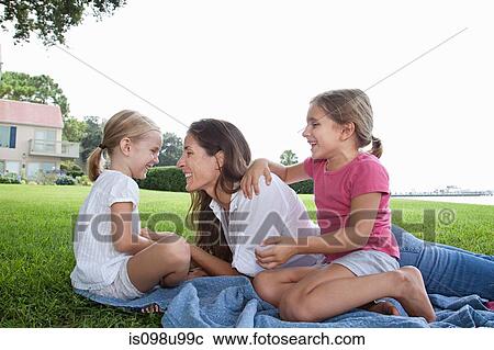 Stock Image - Happy mother and daughters lying on grass. Fotosearch