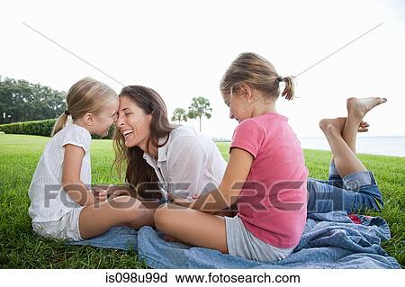 Stock Image - Happy mother and daughters lying on grass. Fotosearch