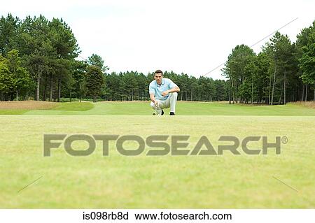 Stock Image - Male golfer crouching on the fairway. Fotosearch